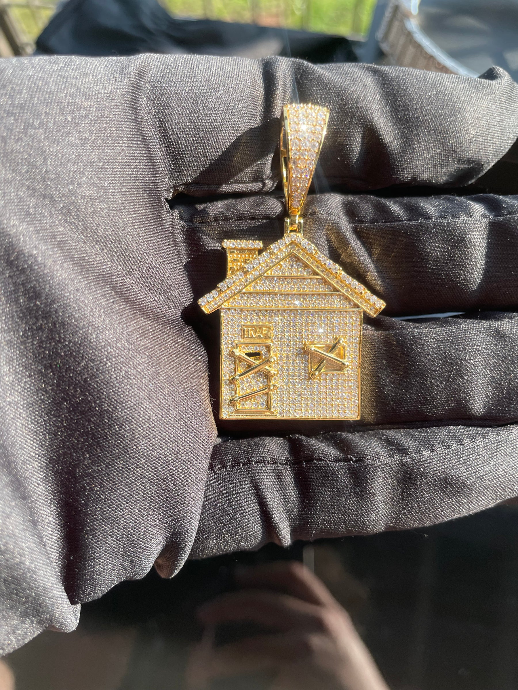 Trap house pendant held in hand showing the stone-set front and bail