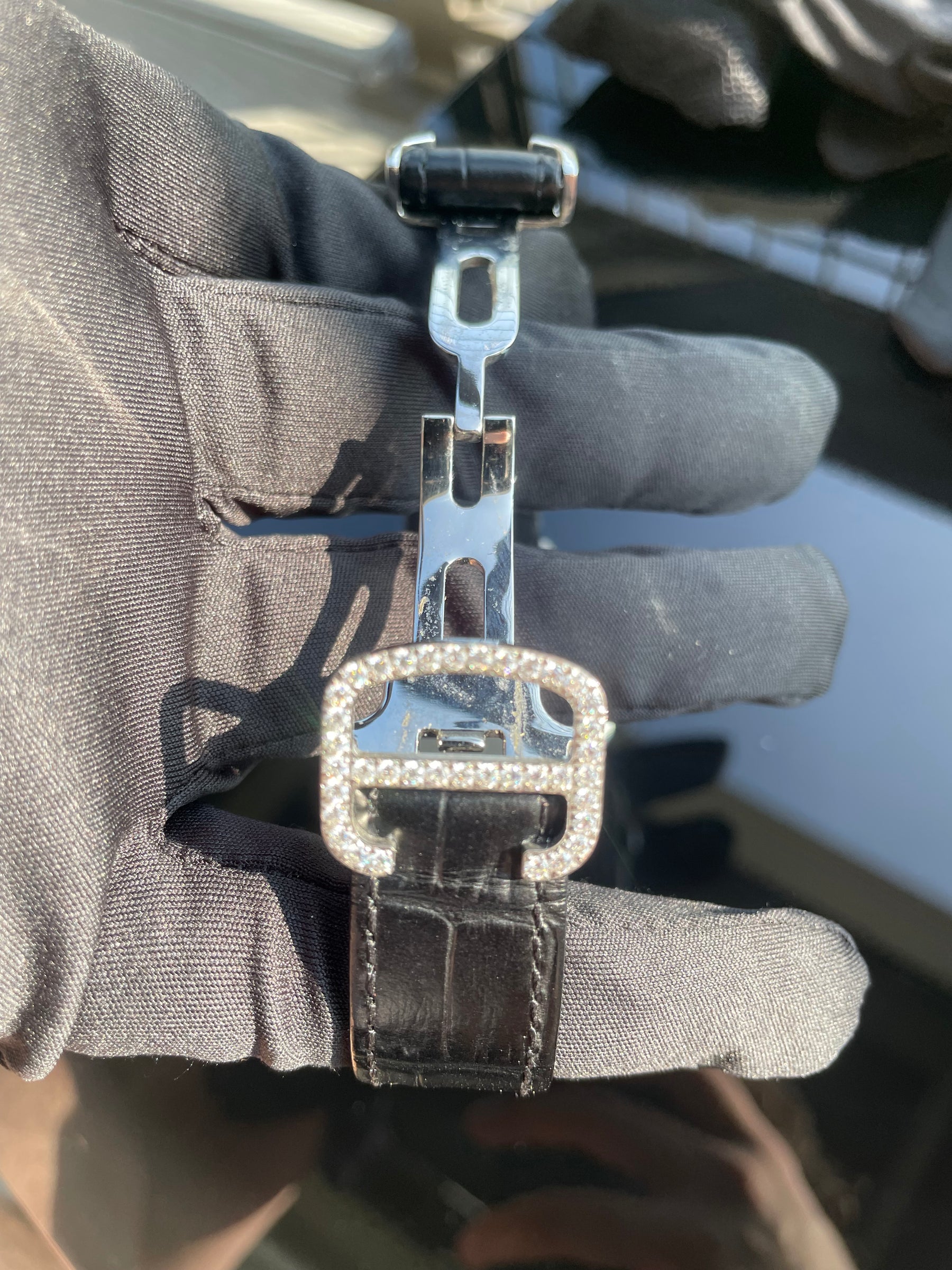 Stone-set deployant buckle on the black leather watch strap